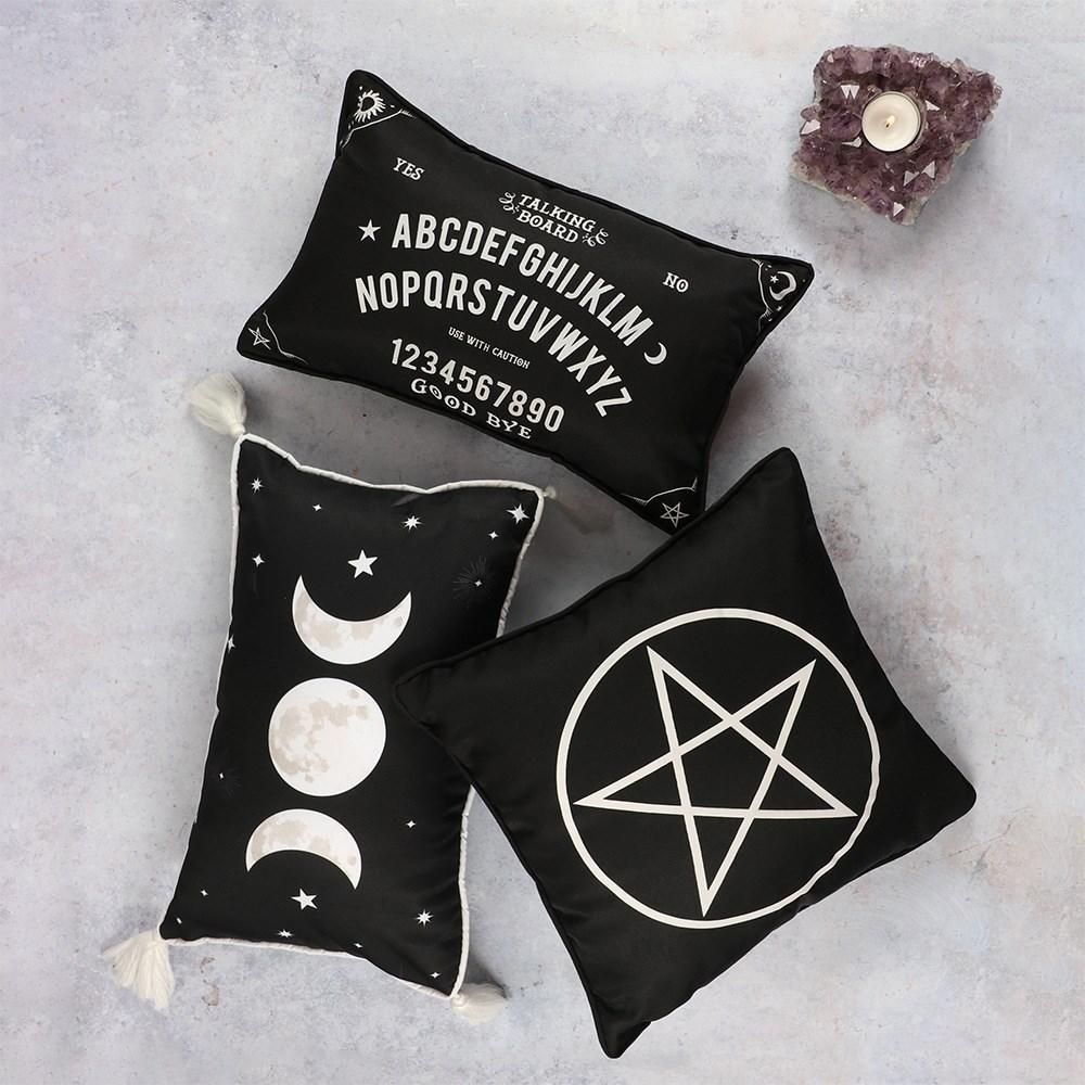 Black square cushion with single white pentagram design, shown amongst other cushions with similar designs.