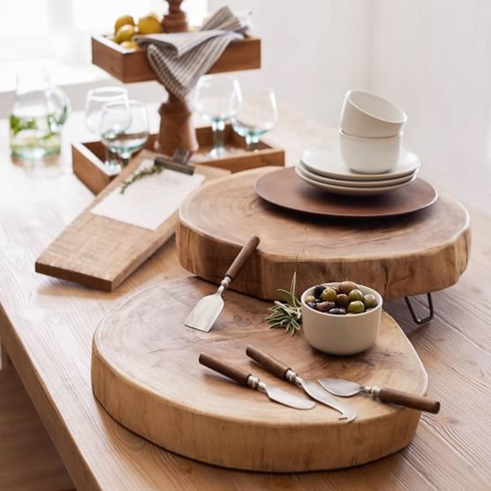 Two round wooden serving boards and tiered serving stand with plates, olives, wine glasses, napkins and cheese knives.