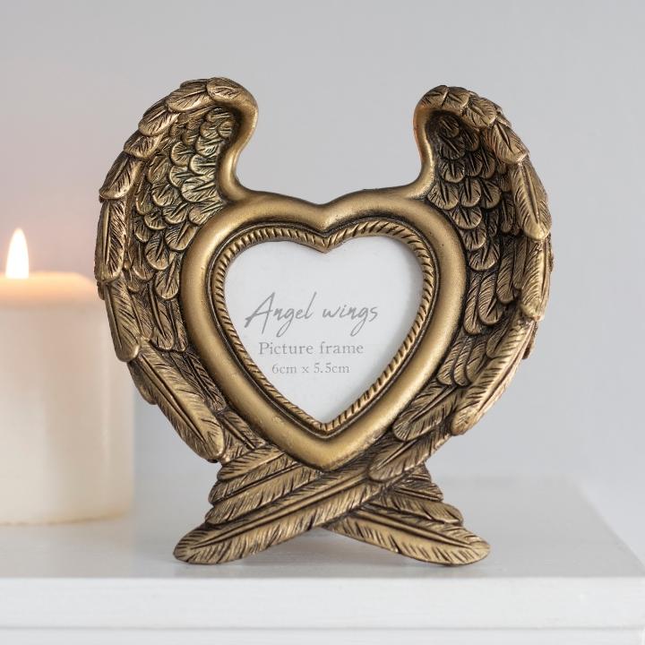 Antique gold guardian angel wing photo frame with a heart-shaped window, with a white background and a lit pillar candle.