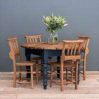 Rustic round wooden farmhouse dining table and four chairs with navy blue legs, with a glass vase of white lilies on top.