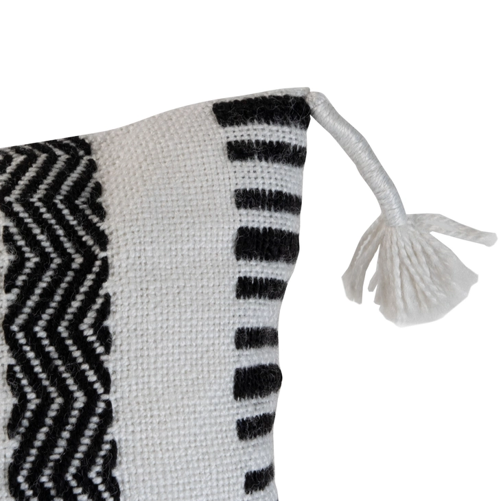 A hand woven outdoor boho cushion with a patterned mix of black and white yarns, close up shows thread wrapped corner tassel.