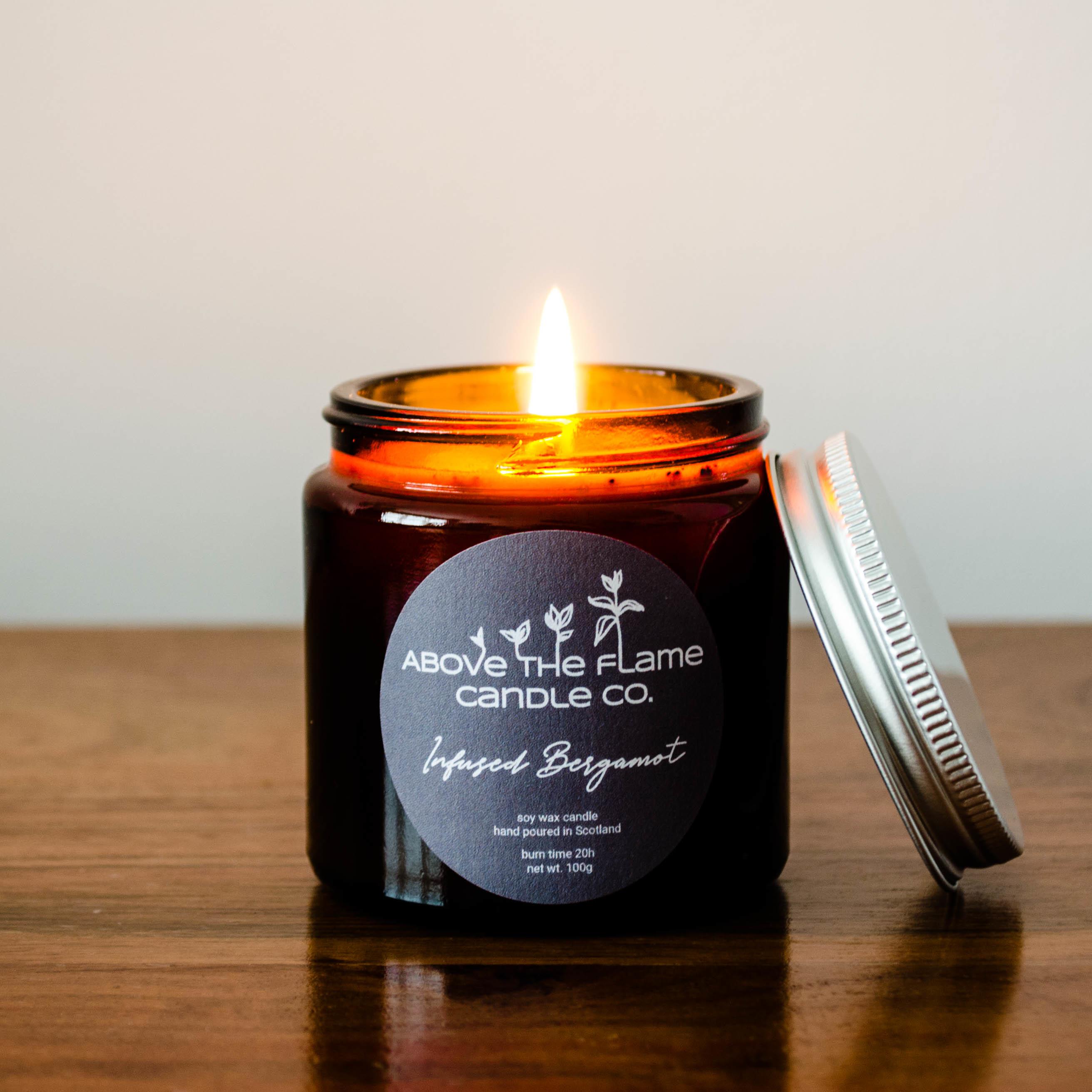A lit infused bergamot amber soy wax candle jar handmade by above the flame candle Co on a wooden table