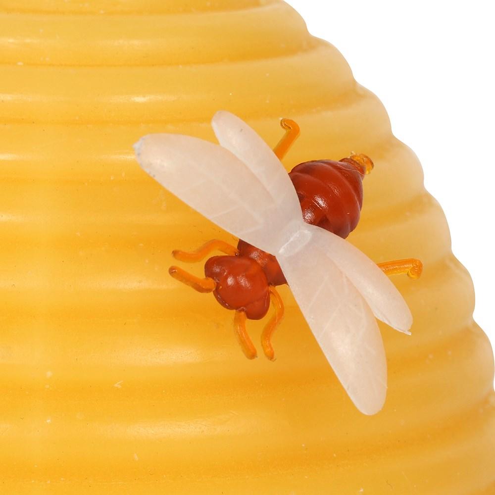 Yellow beeswax hive shaped candle with a bee on the side, close up of bee.