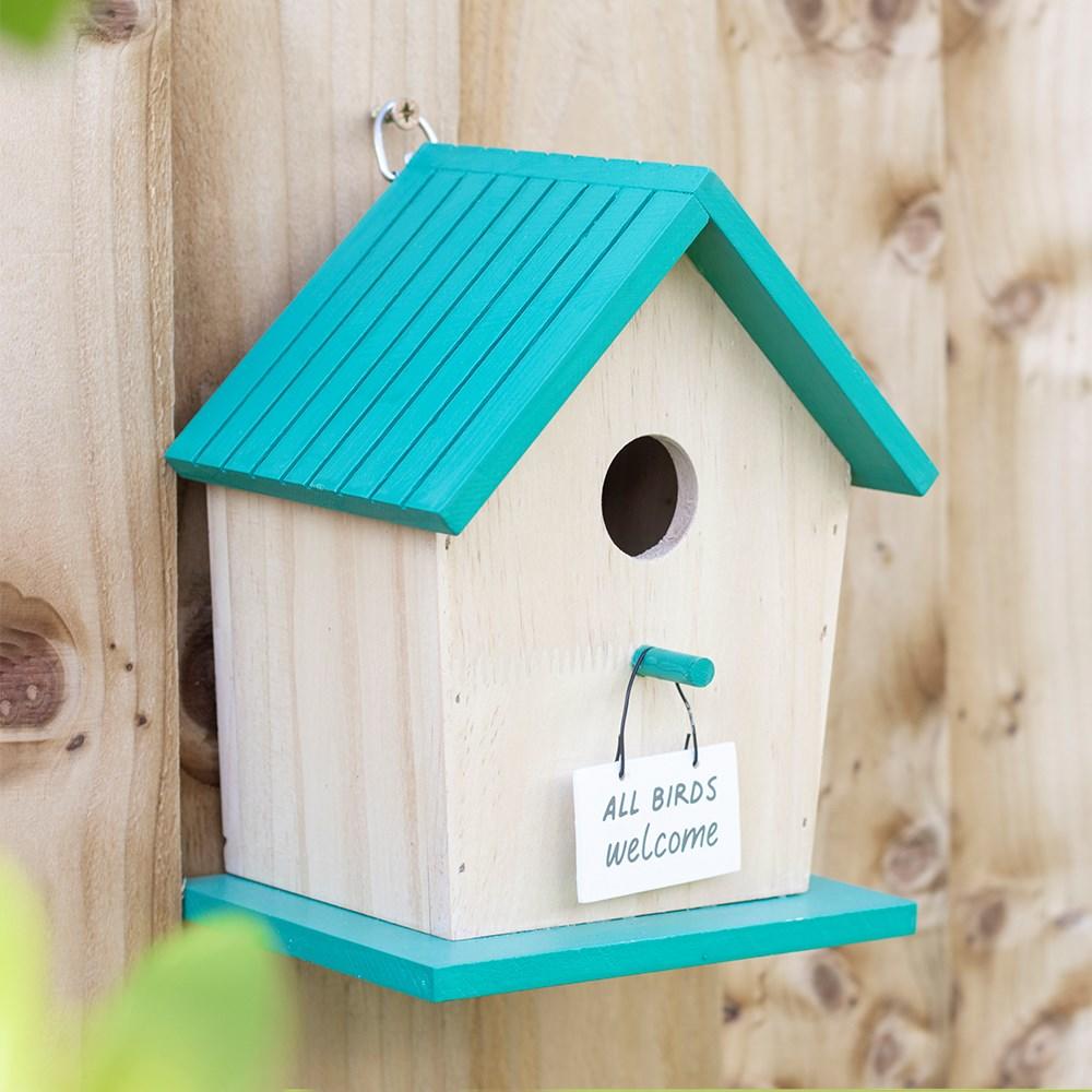 Wooden birdhouse with 'All Birds Welcome' text, blue roof and base, hung on a tree.