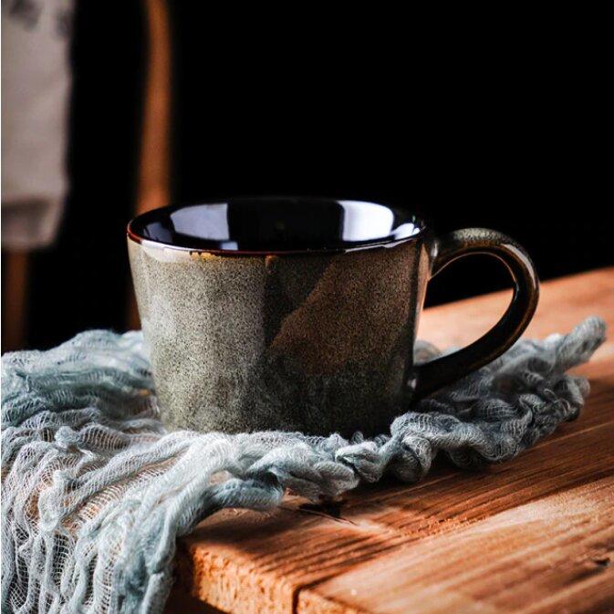 Dark grey handmade retro ceramic mug, on a blue woven material on a wooden surface.