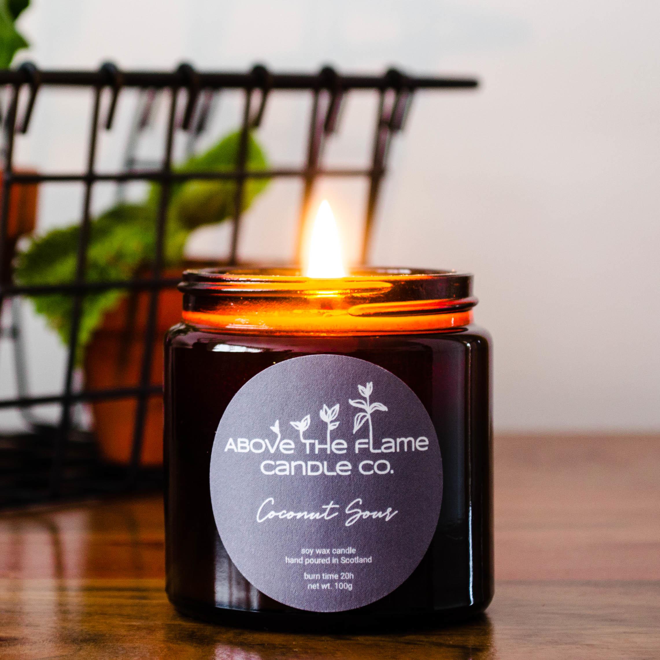 A lit coconut sour amber soy wax candle jar handmade by above the flame candle Co on a wooden table
