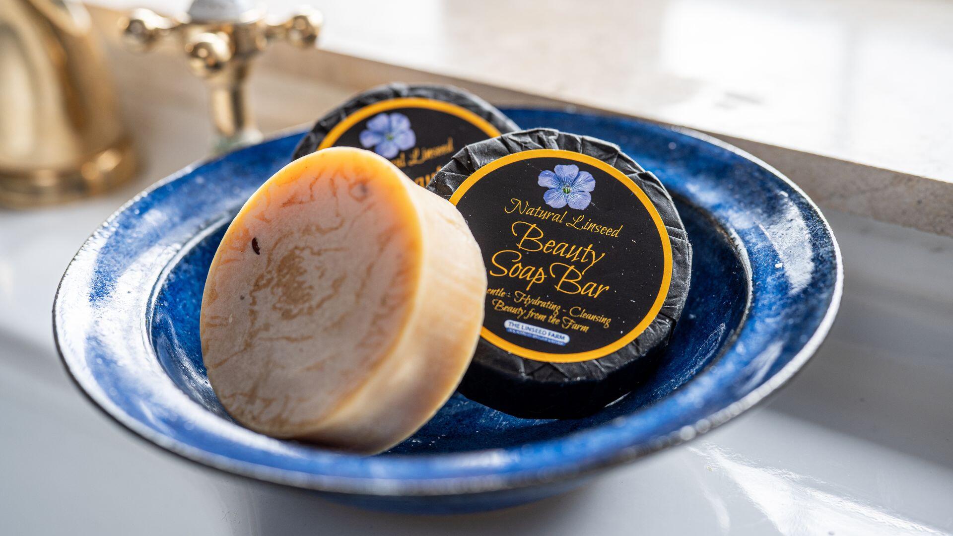 A blue dish on a bathroom sink containing 3 round bars of Natural Linseed beauty soap.