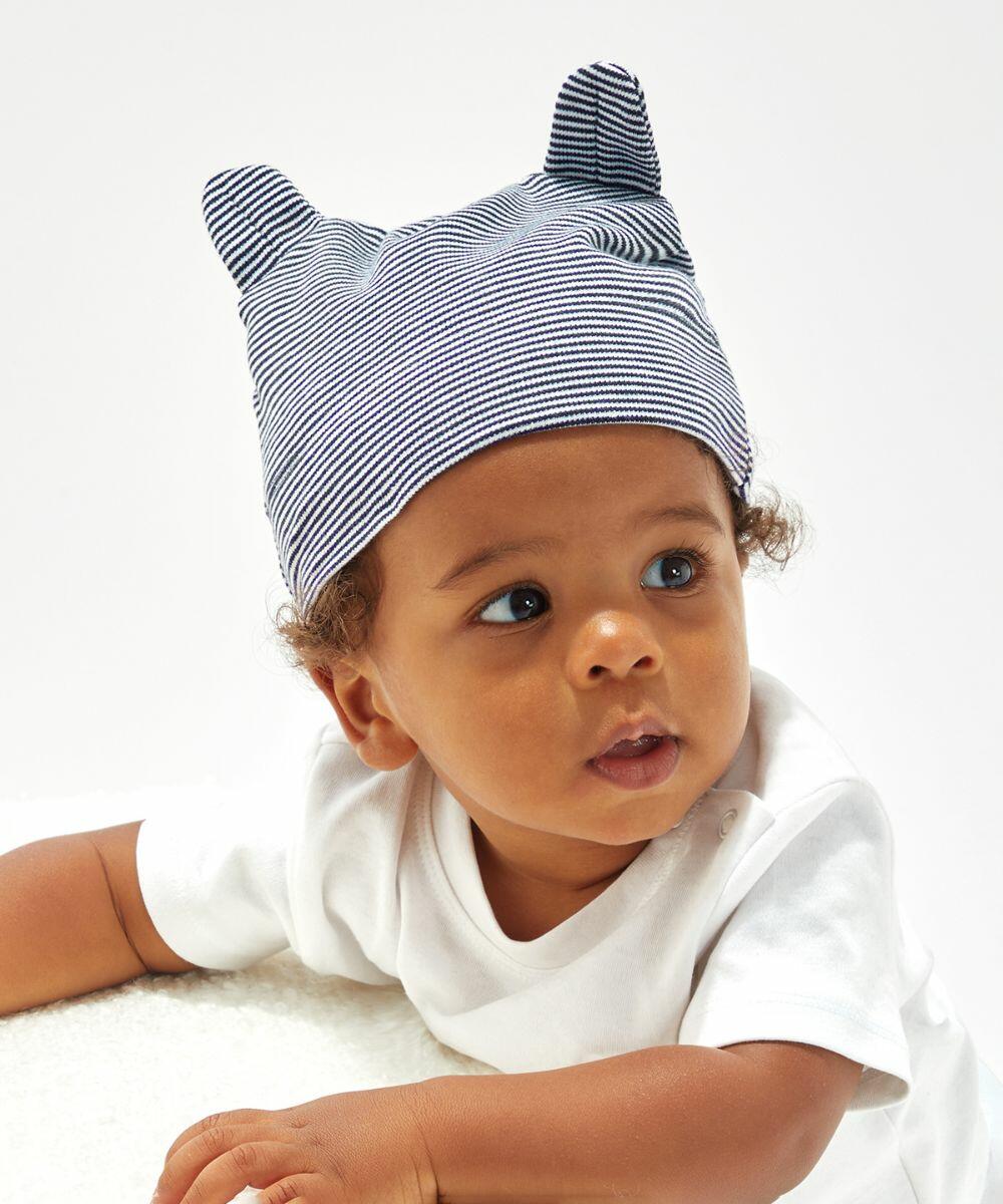 A baby wearing a white Babybugz BZ051 shirt and a striped hat with two small, pointed peaks looks to the side.