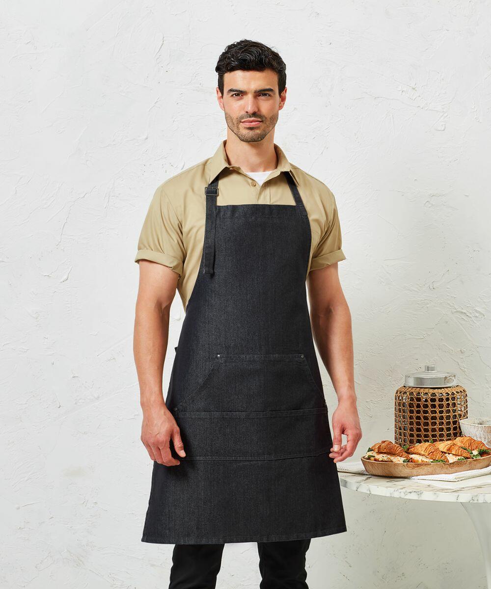 A man stands wearing a beige shirt and a dark apron in front of a light textured background. A table with Premier PR126 and a jar is visible beside him.
