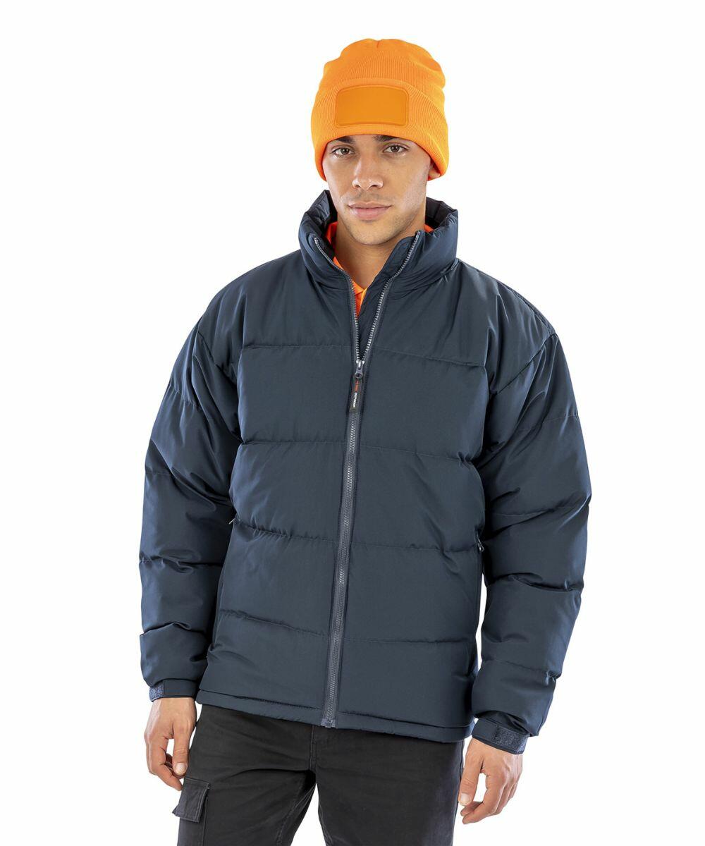 A person wearing an orange beanie, a dark Result R181M puffer jacket, and dark pants, standing against a white background.