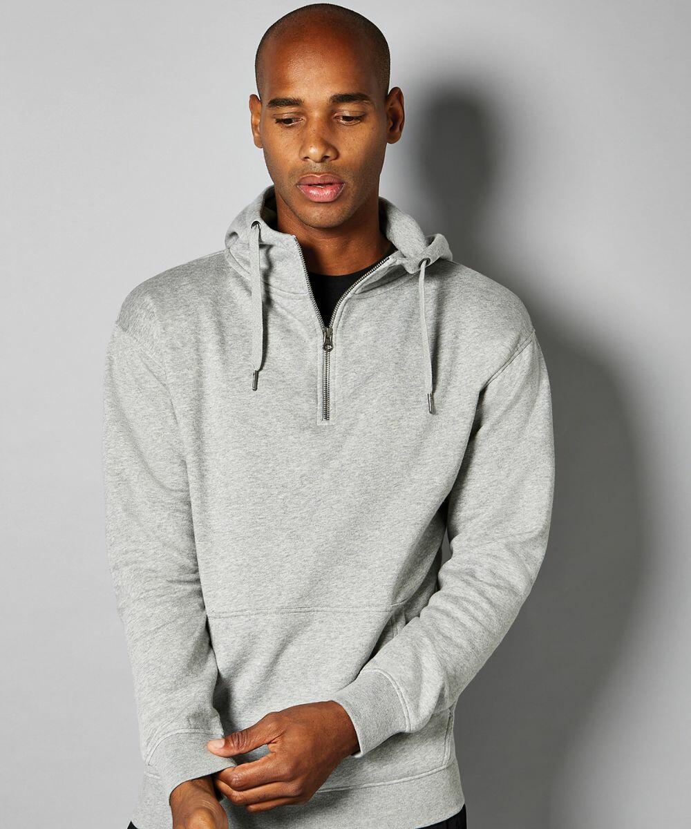A man wearing a grey KK336 hoodie by Kustom Kit stands against a plain background, looking down with his hands clasped.