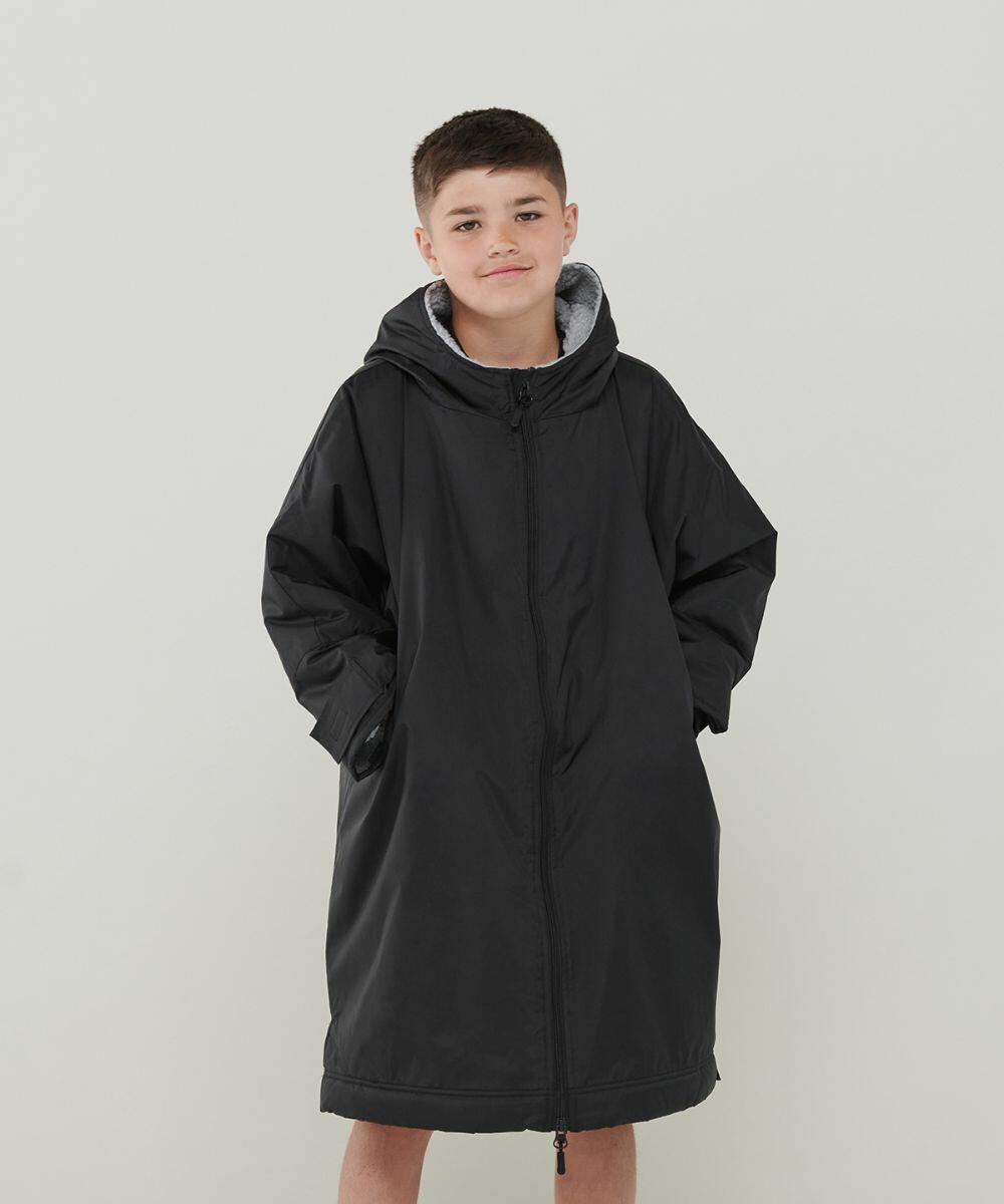A young boy stands with his hands in the pockets of a long, black hooded coat. He has short hair and is wearing a neutral expression. The background is plain white. The coat he is wearing is the LV691 from Finden & Hales.