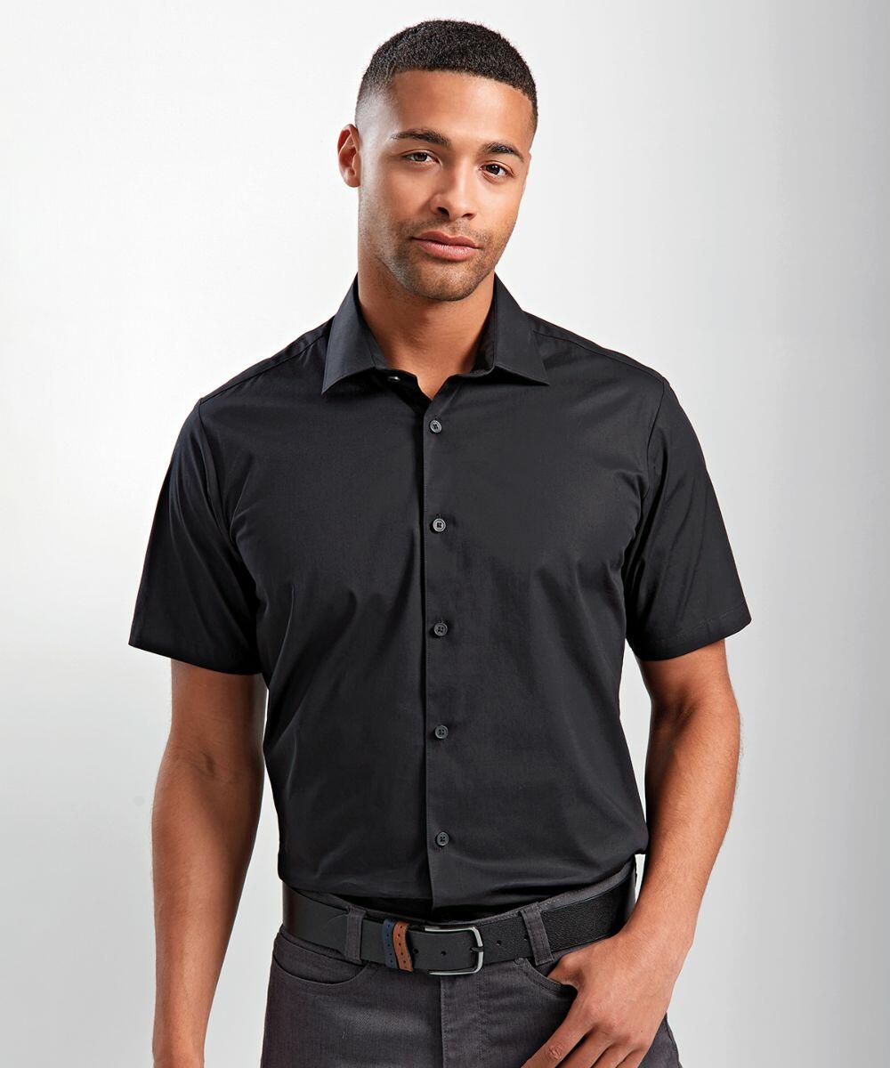 A man wearing a black Premier PR246 short-sleeved button-up shirt and dark gray pants stands against a plain background.