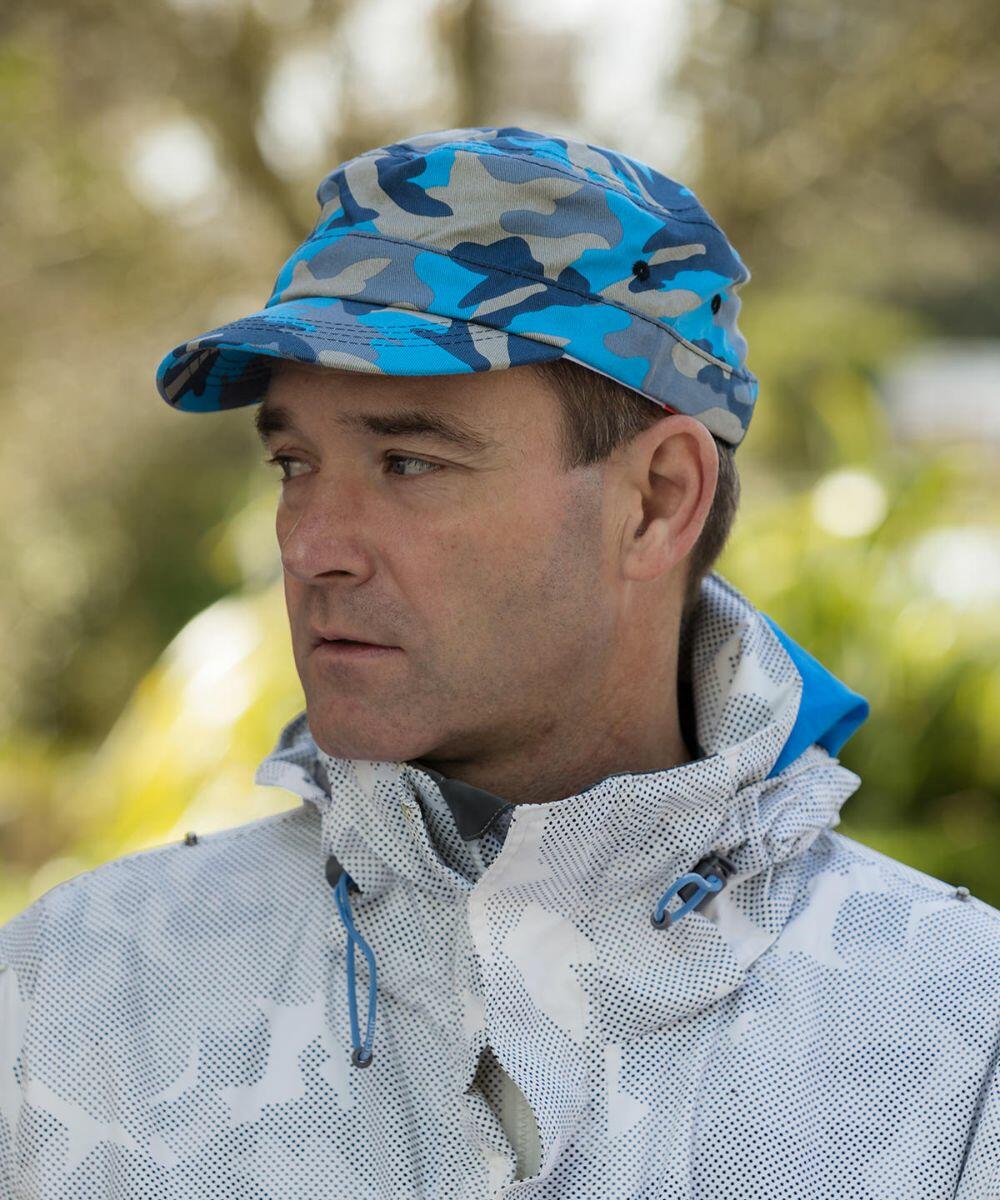 Man in a blue and gray camouflage cap and a light-colored Result RC59X jacket with blue accents, standing outdoors with greenery in the background.