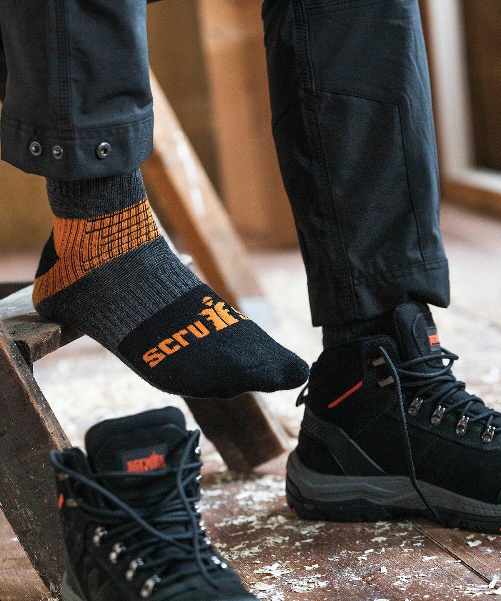 Person wearing mismatched socks, one black and orange with lettering, the other plain black, with black Scruffs SH030 cargo pants and black hiking shoes.