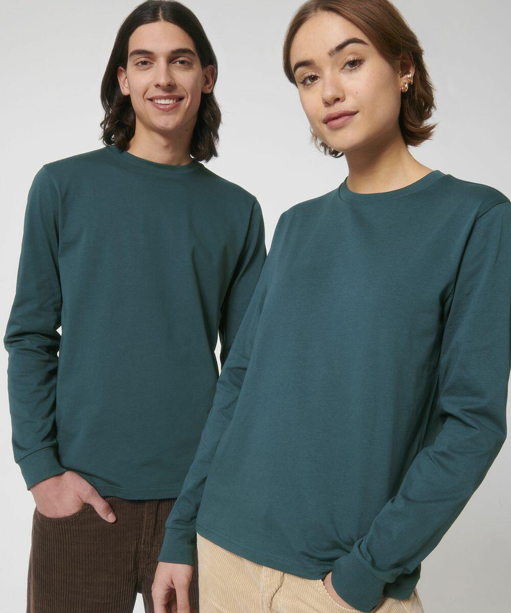 Two people stand side by side, both wearing long-sleeved green shirts from Stanley/Stella called the SX053. The person on the left has hands in pockets and is smiling, while the person on the right has a neutral expression.