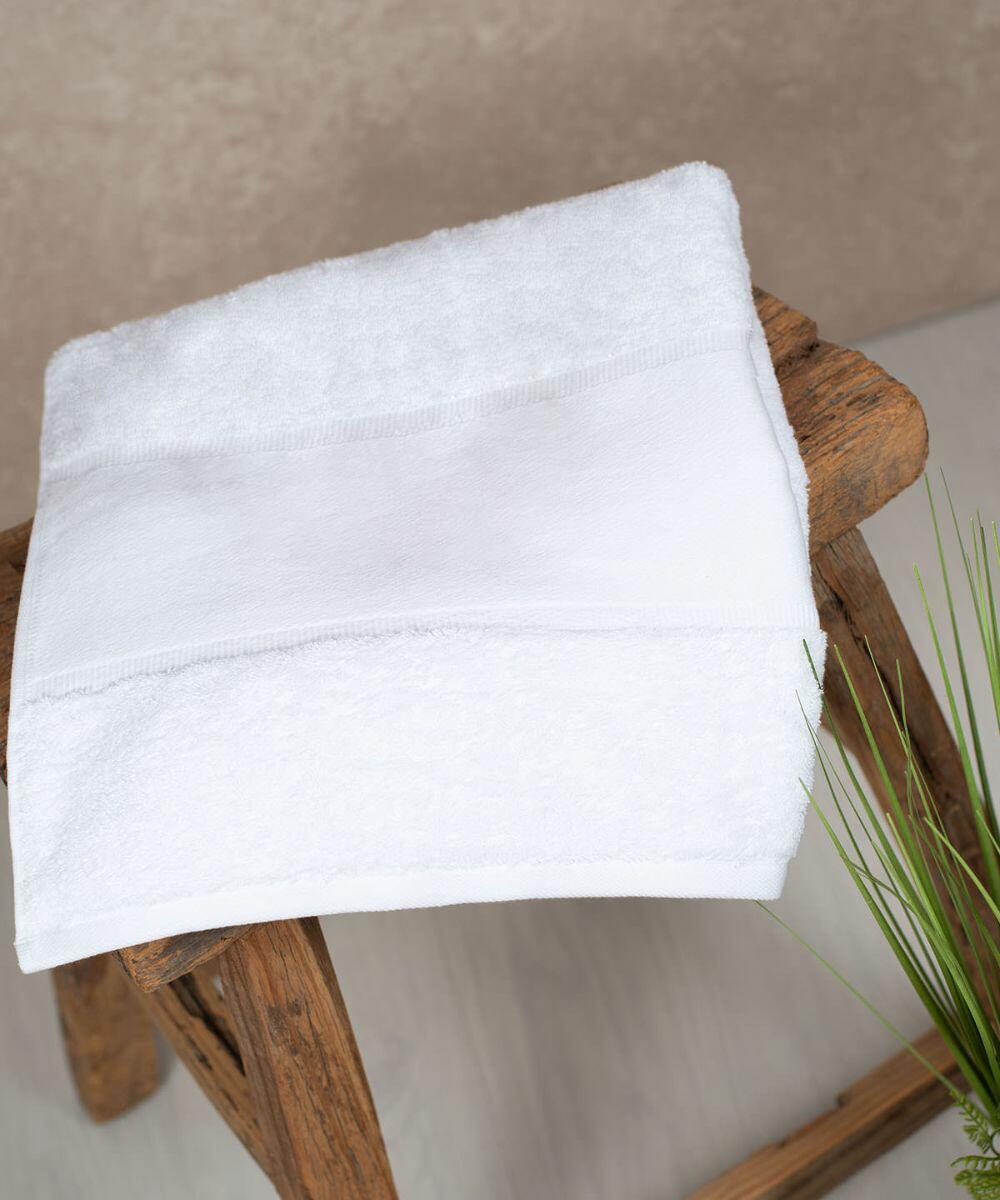 A Towel City TC504 is neatly folded and placed on a rustic wooden stool next to a green plant.