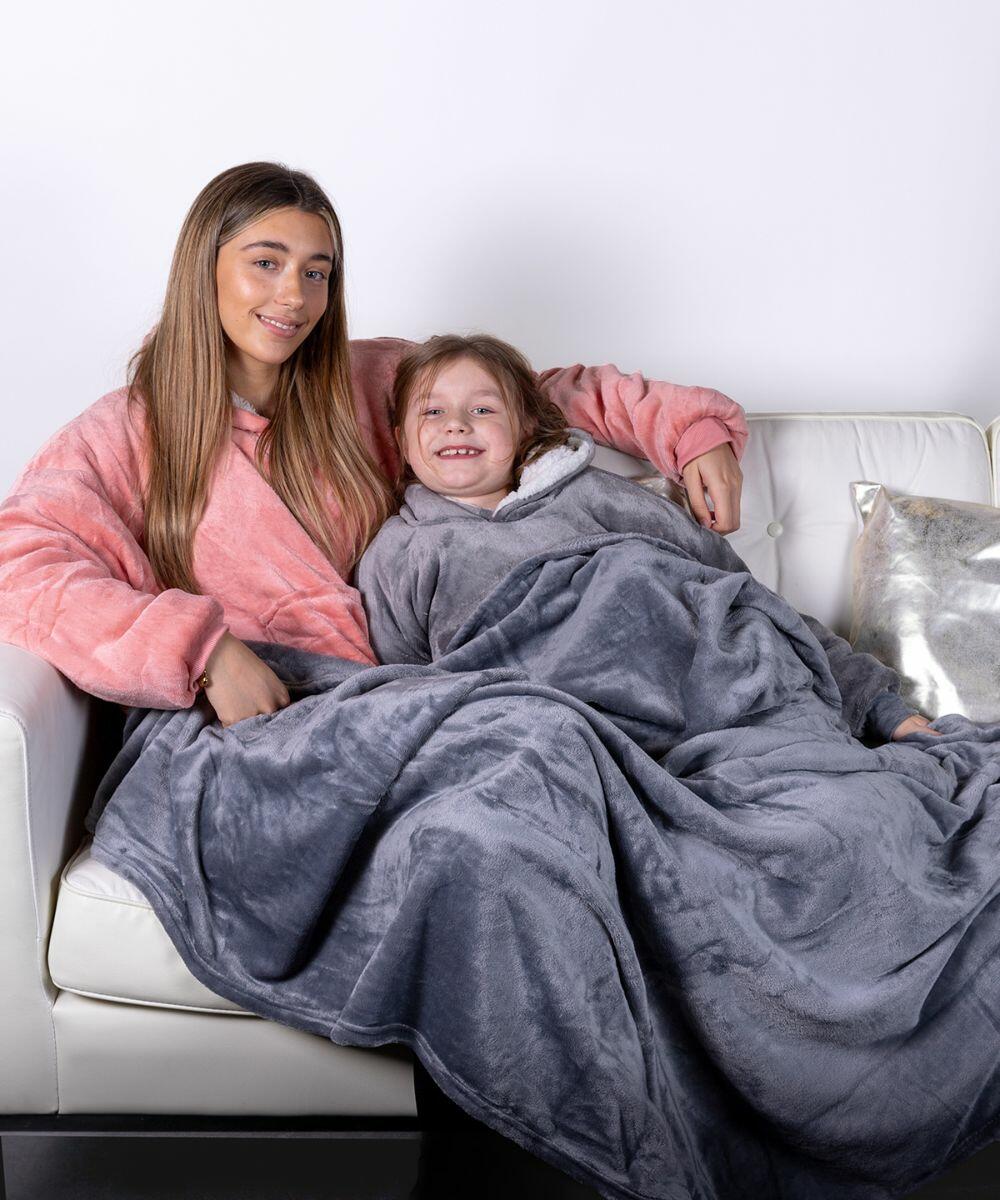 Two people sitting on a white couch, covered with grey and pink Ribbon RI014 fleece blankets, smiling at the camera.