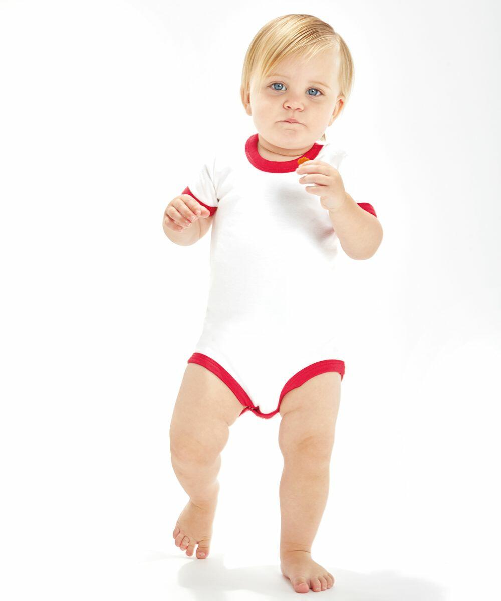 A toddler with blond hair is standing and walking towards the camera, wearing a white Babybugz BZ019 onesie with red trim, holding a small object in one hand.