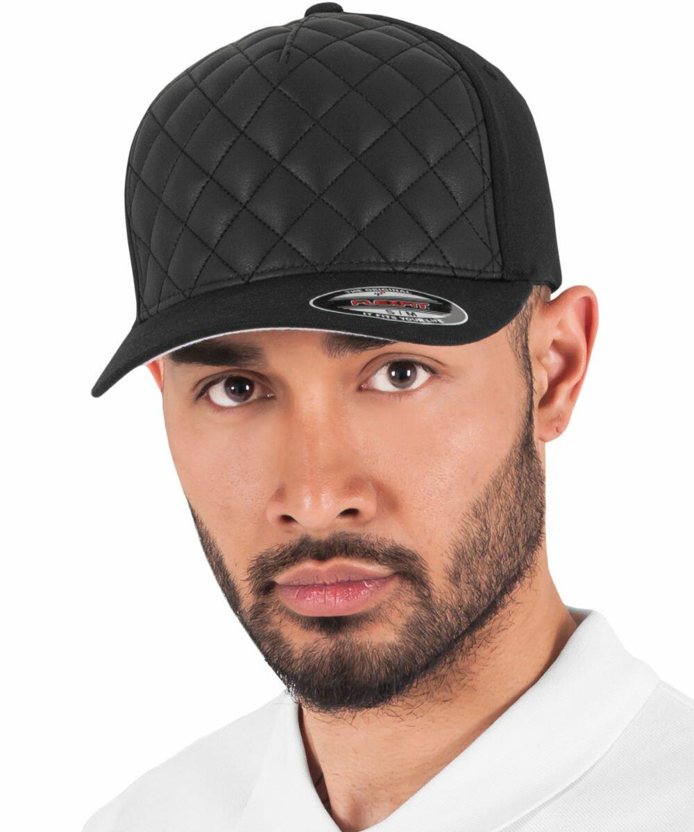 A person with a beard and mustache wears a black, quilted Flexfit By Yupoong YP118 baseball cap and a white shirt, looking directly at the camera.