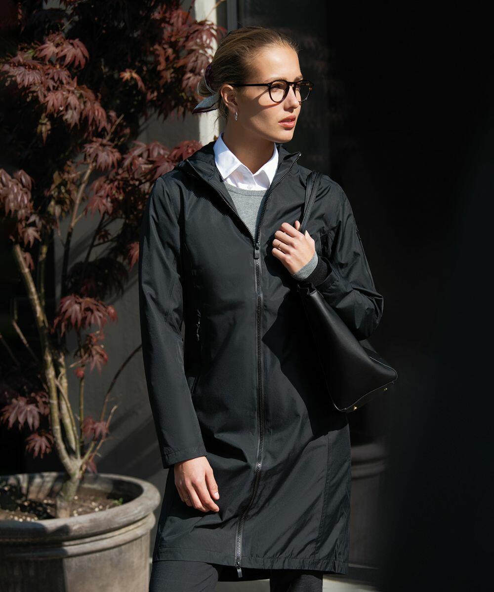 A person wearing a Nimbus NB97F jacket and glasses stands in front of a building with potted plants, looking to the side.