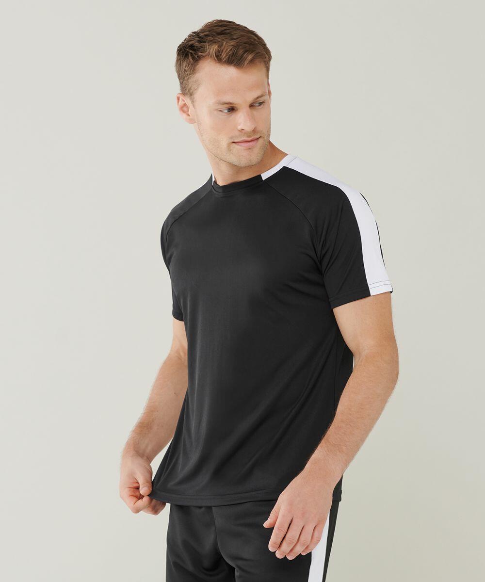 A man in a black and white Finden & Hales LV290 sports t-shirt and black pants stands against a plain background, looking to his left while holding the hem of his shirt.