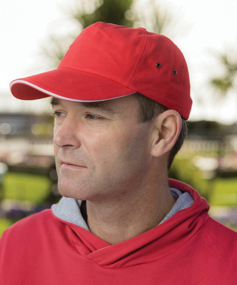 A man wearing a Result RC72X red cap and a matching hoodie looks into the distance outdoors.