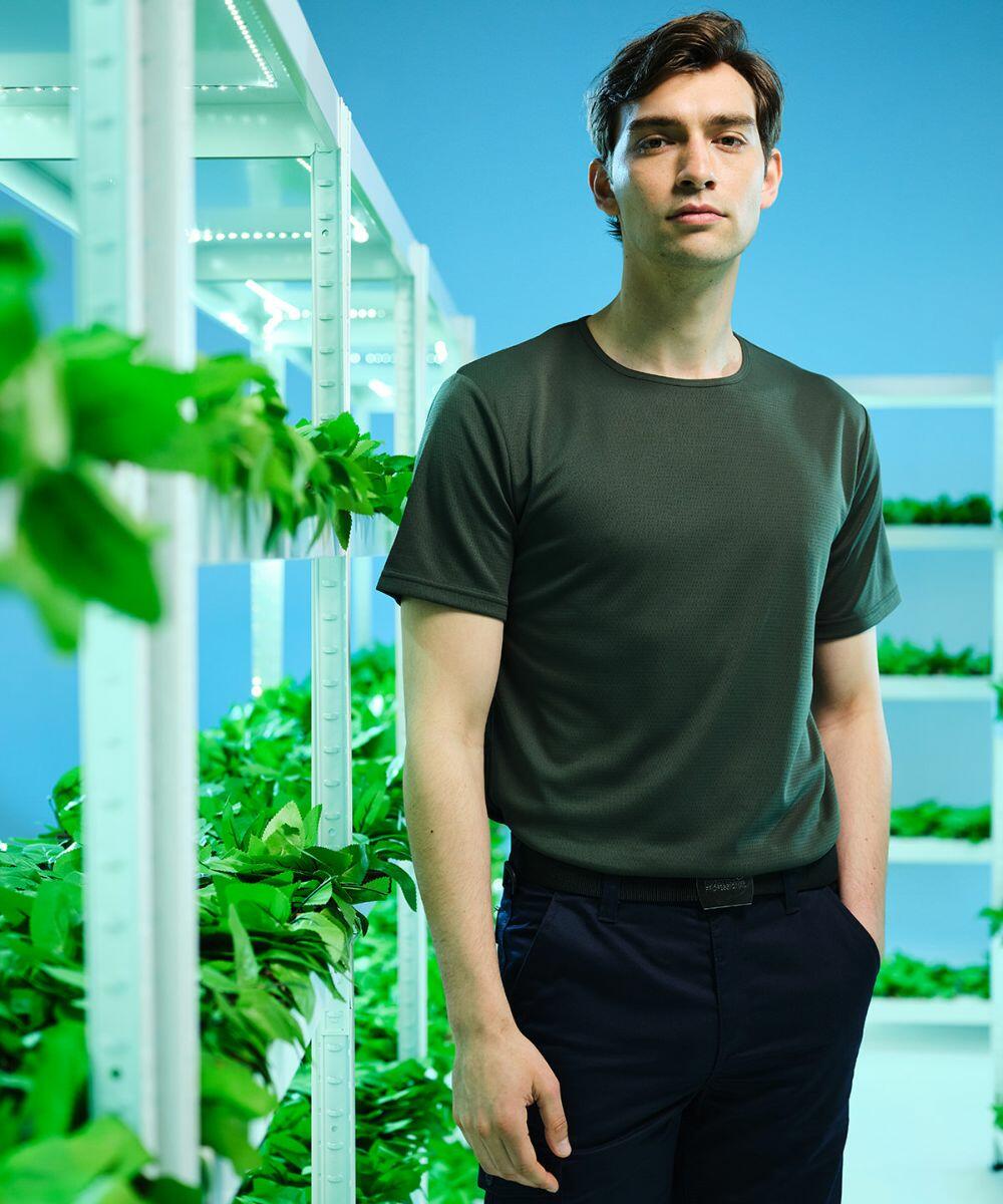 A man stands in a room with vertical plant shelves on both sides, wearing a dark green Regatta RG619 t-shirt and dark pants, with a light blue background.