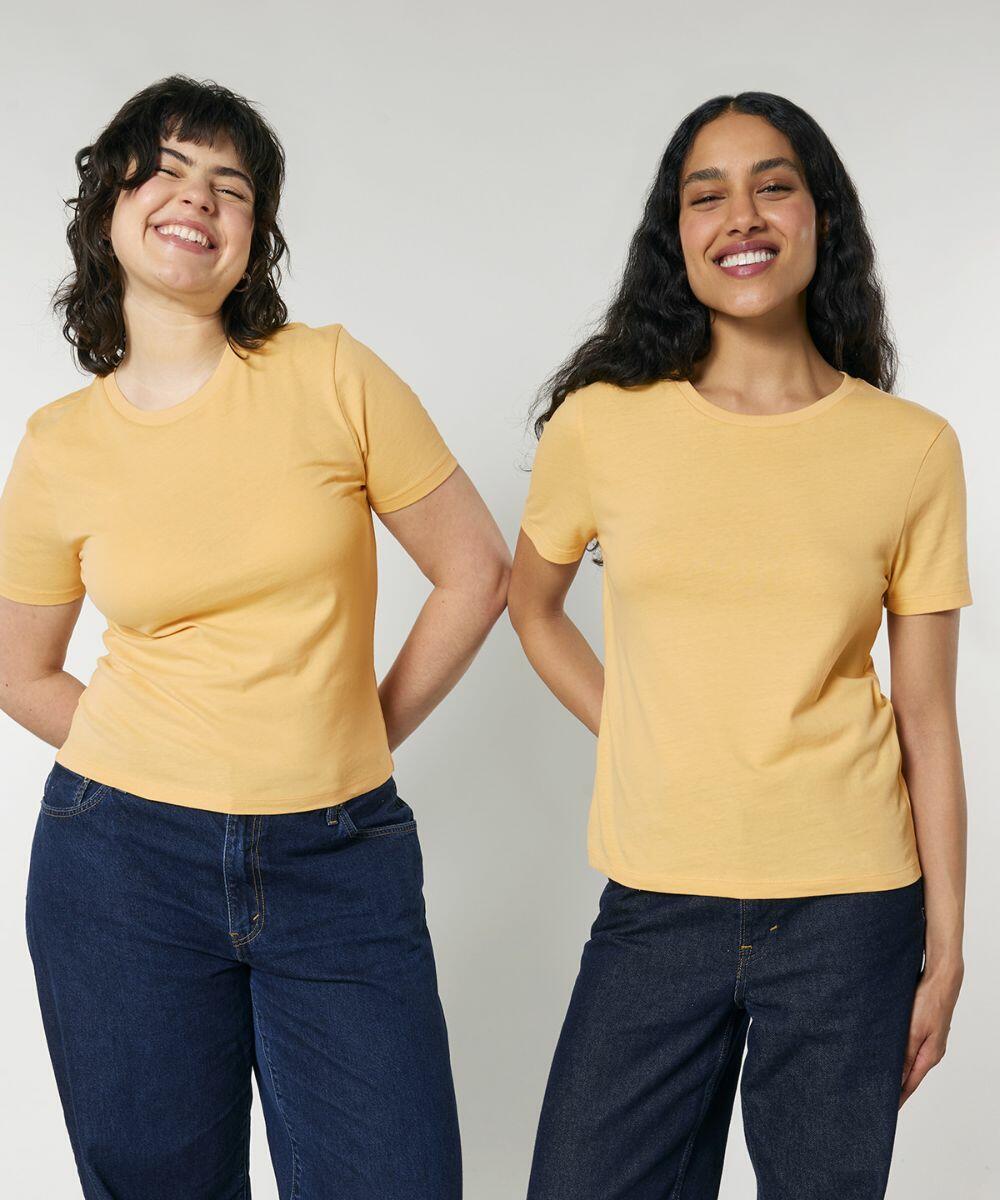 Two women stand side by side, smiling and wearing yellow SX234 t-shirts by Stanley/Stella and dark jeans against a plain background.