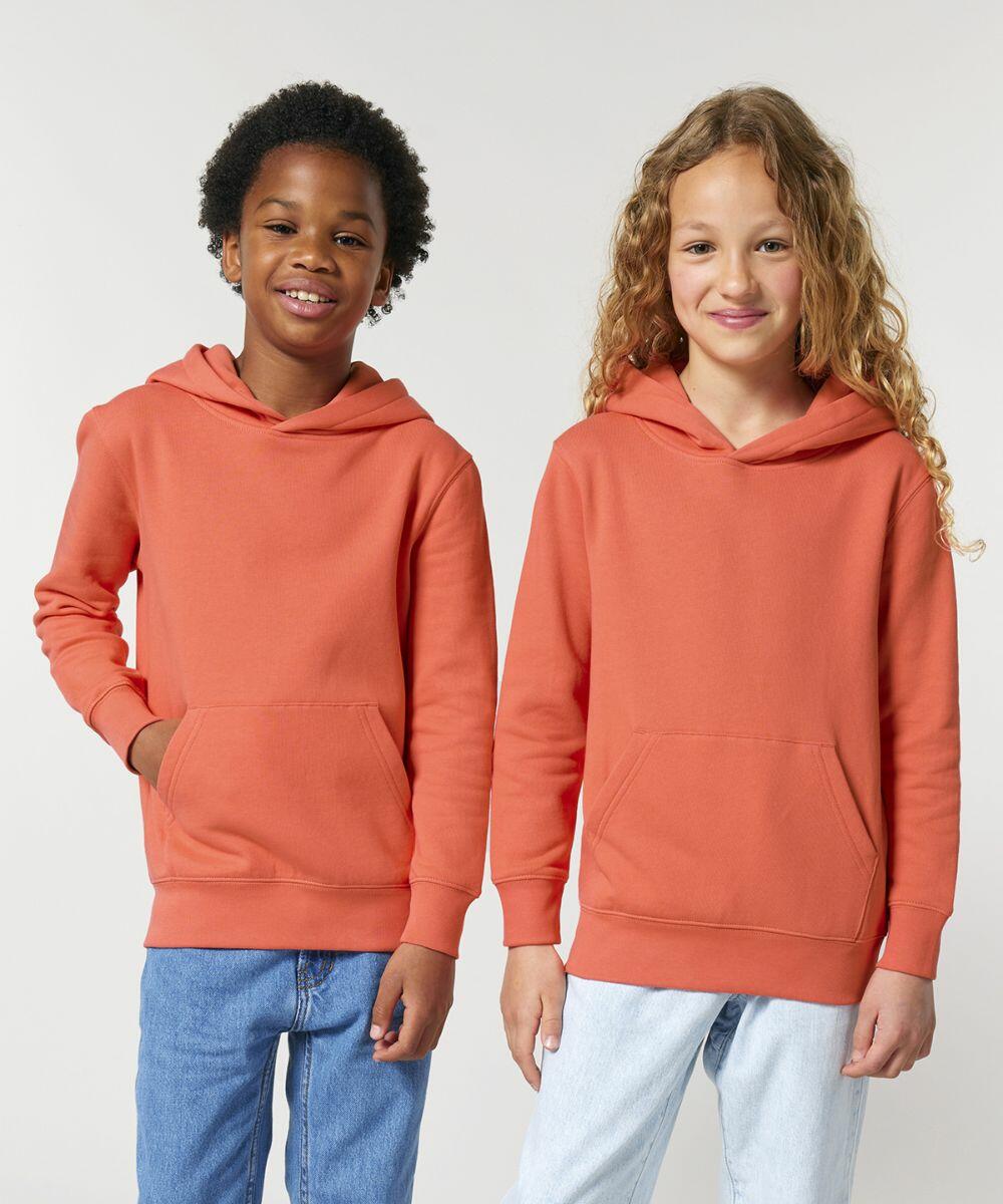 Two children are standing side by side, each wearing a Stanley/Stella SX706 orange hoodie and blue jeans. They are both smiling and looking at the camera.