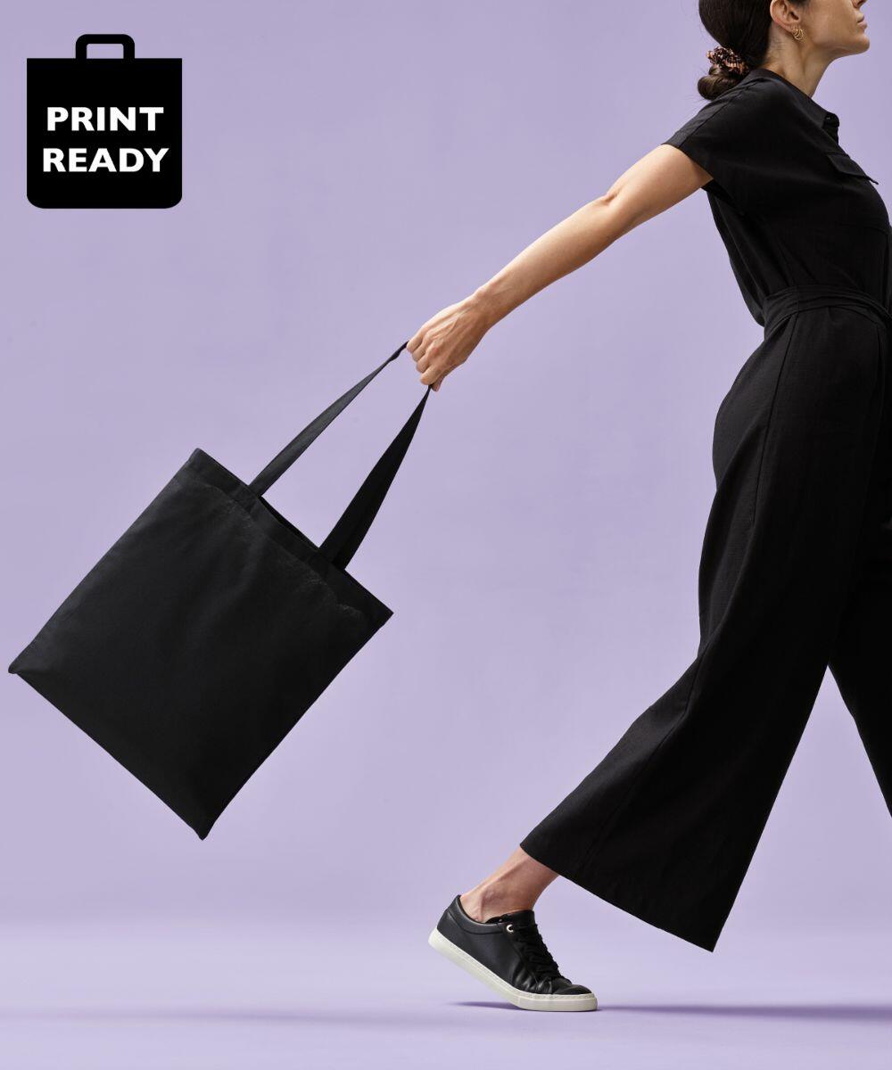 A person wearing a black outfit and black shoes is carrying a black Nutshell RL100 against a purple background. "PRINT READY" is written in a black bag icon at the top left corner.