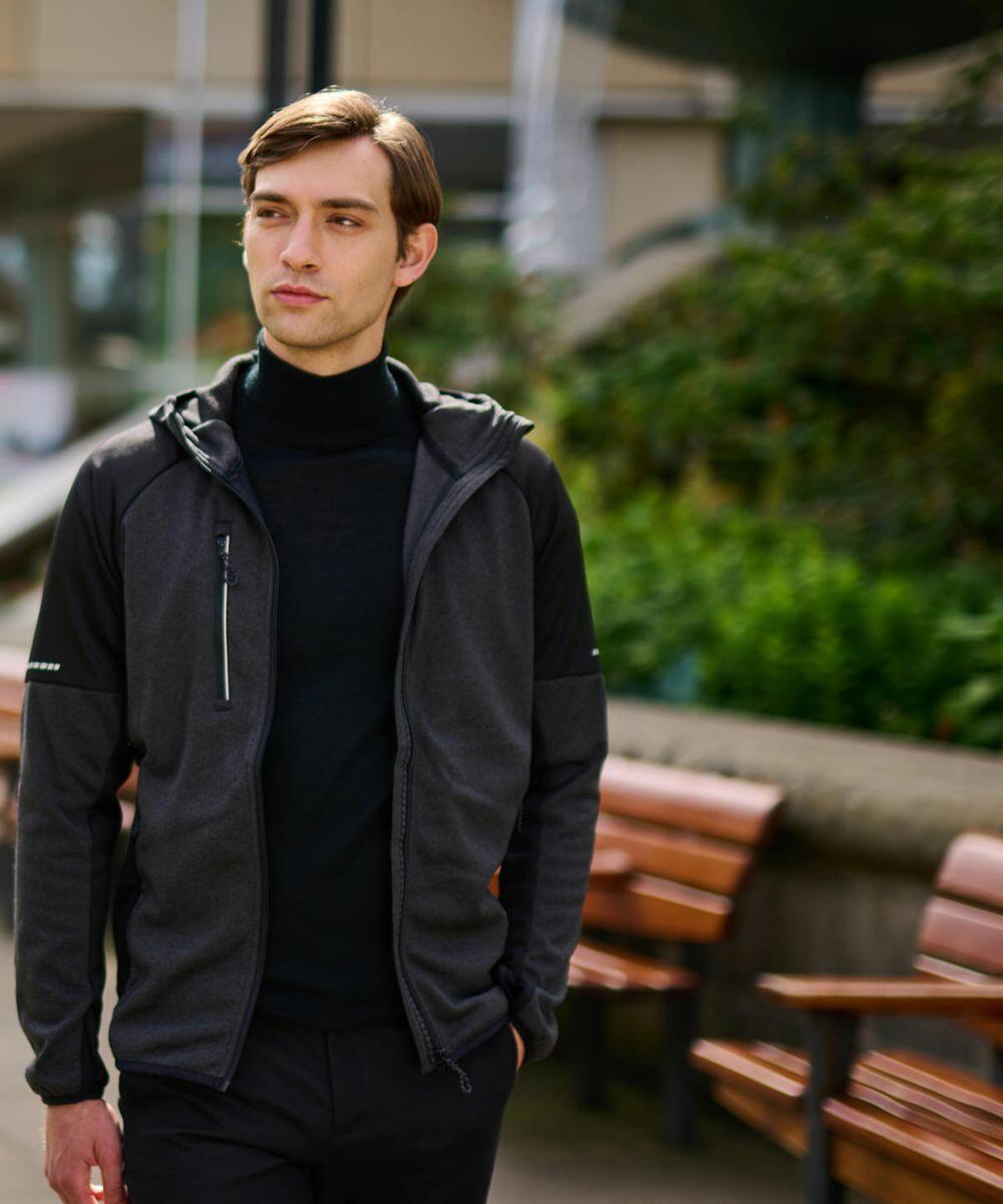 A person wearing a black Regatta RG268 and black turtleneck stands outdoors next to a row of wooden benches.