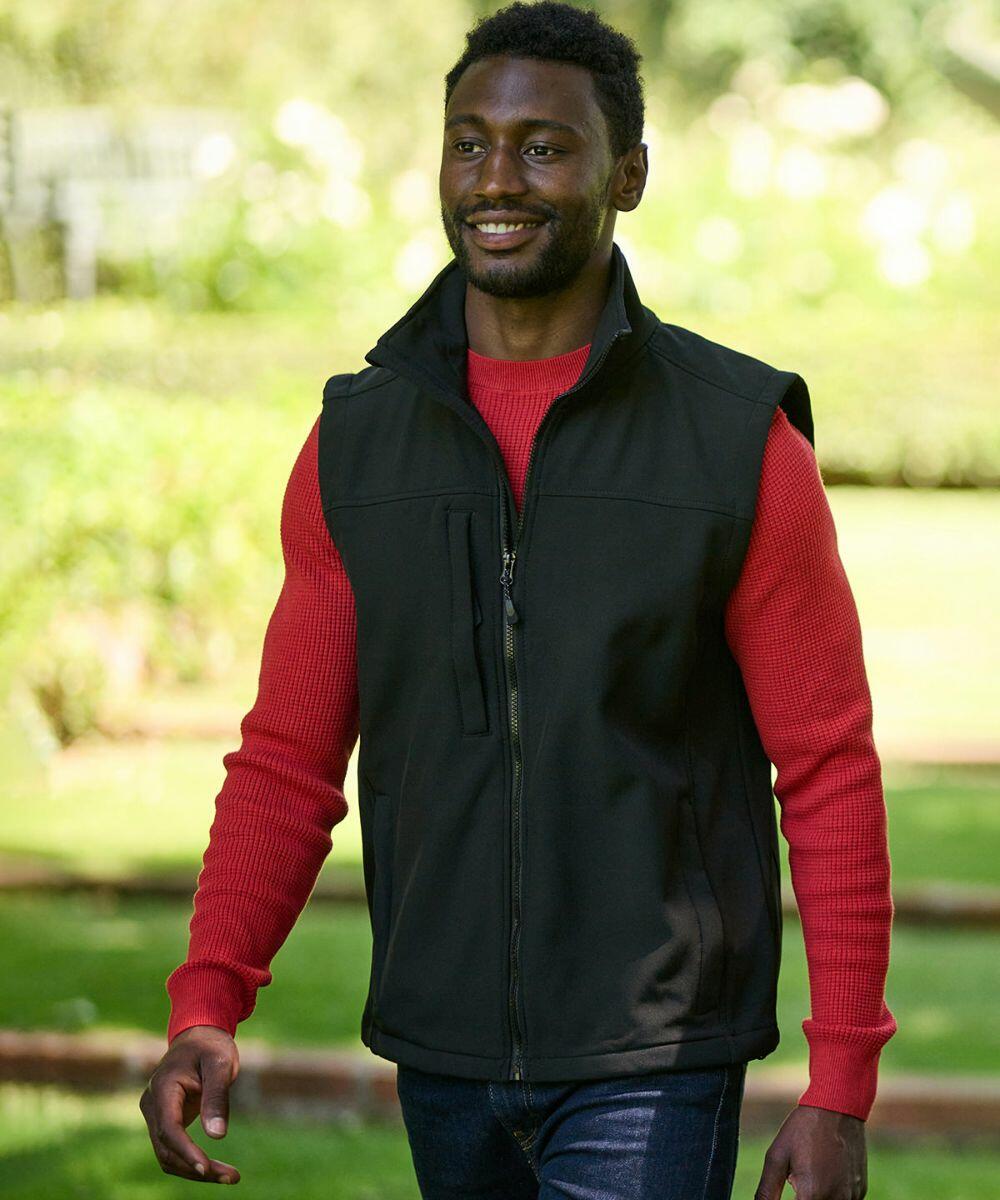 A man wearing a red sweater and a black Regatta RG154 zip-up vest walks outdoors in a garden setting.