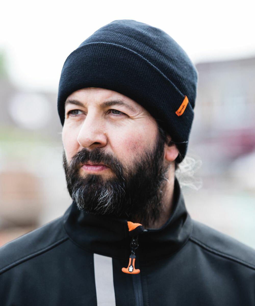 A person with a beard wearing a Scruffs SH084 and black jacket outdoors.