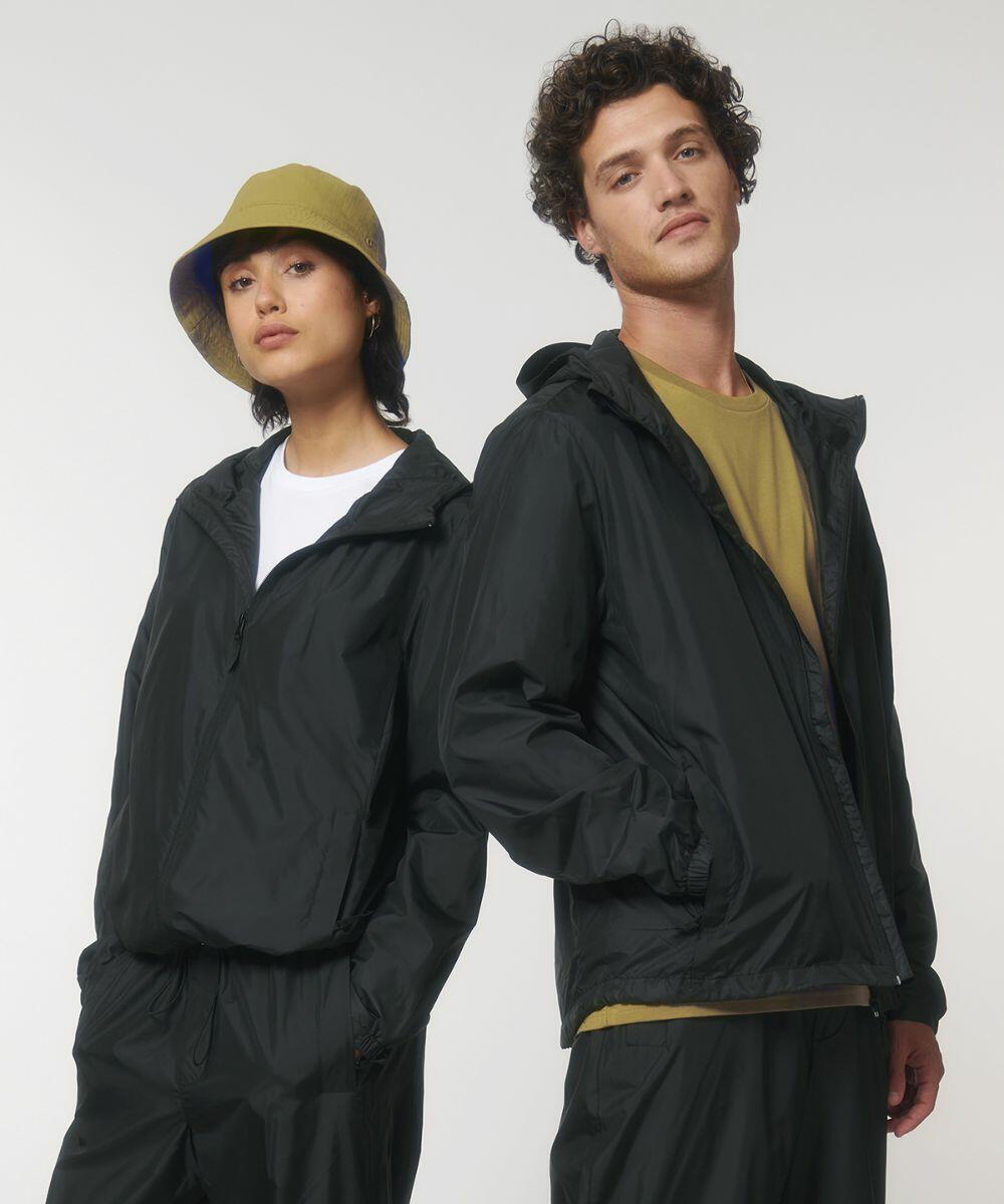 Two individuals in casual attire, wearing black jackets and standing side by side. The person on the left is wearing a yellow SX179 bucket hat by Stanley/Stella. Both have a neutral expression and are facing the camera.