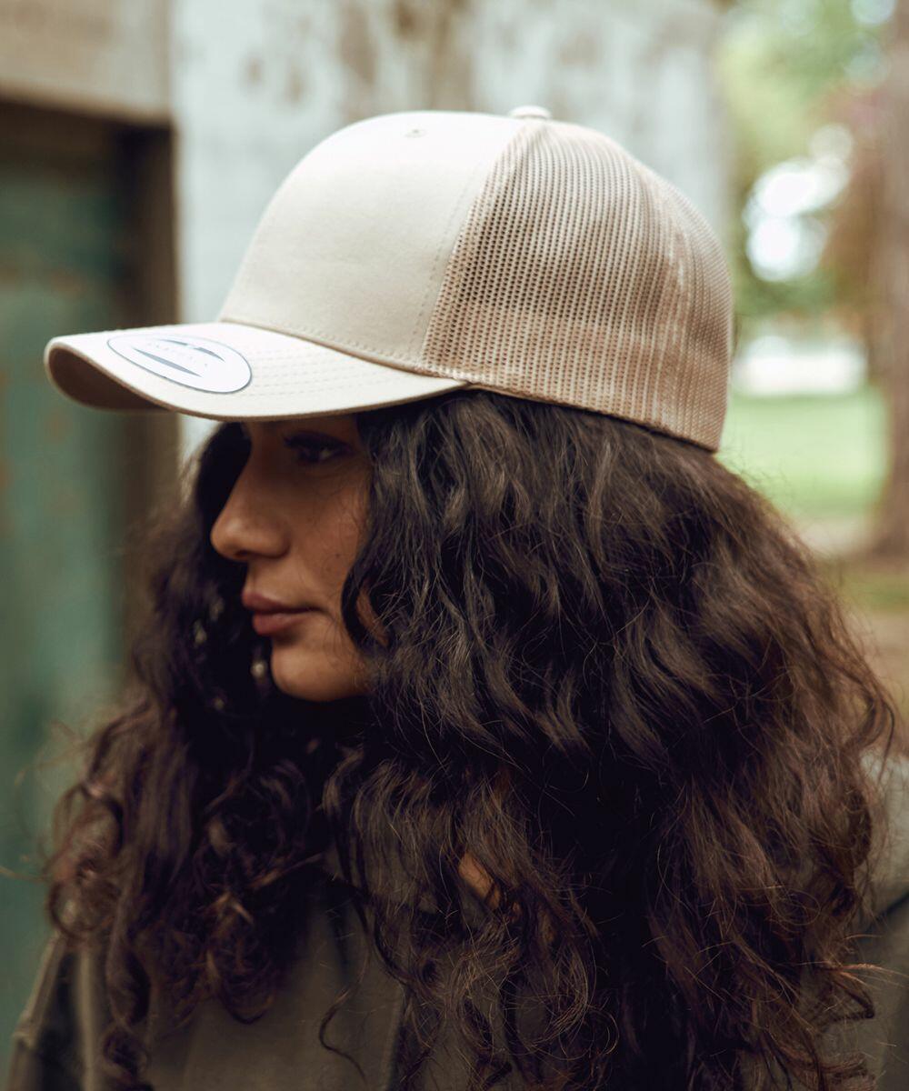 A woman with long curly hair wearing a beige Flexfit By Yupoong YP023 hat looks to the side.