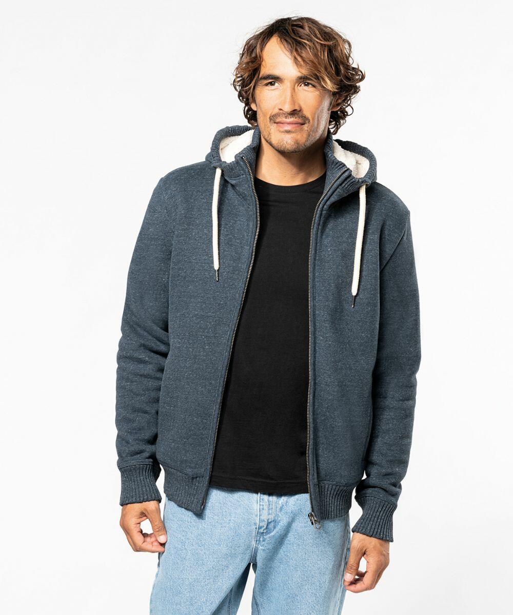 A man with wavy hair is wearing a dark Kariban hoodie with a white drawstring and a black K2312 t-shirt. He is standing against a plain white background.