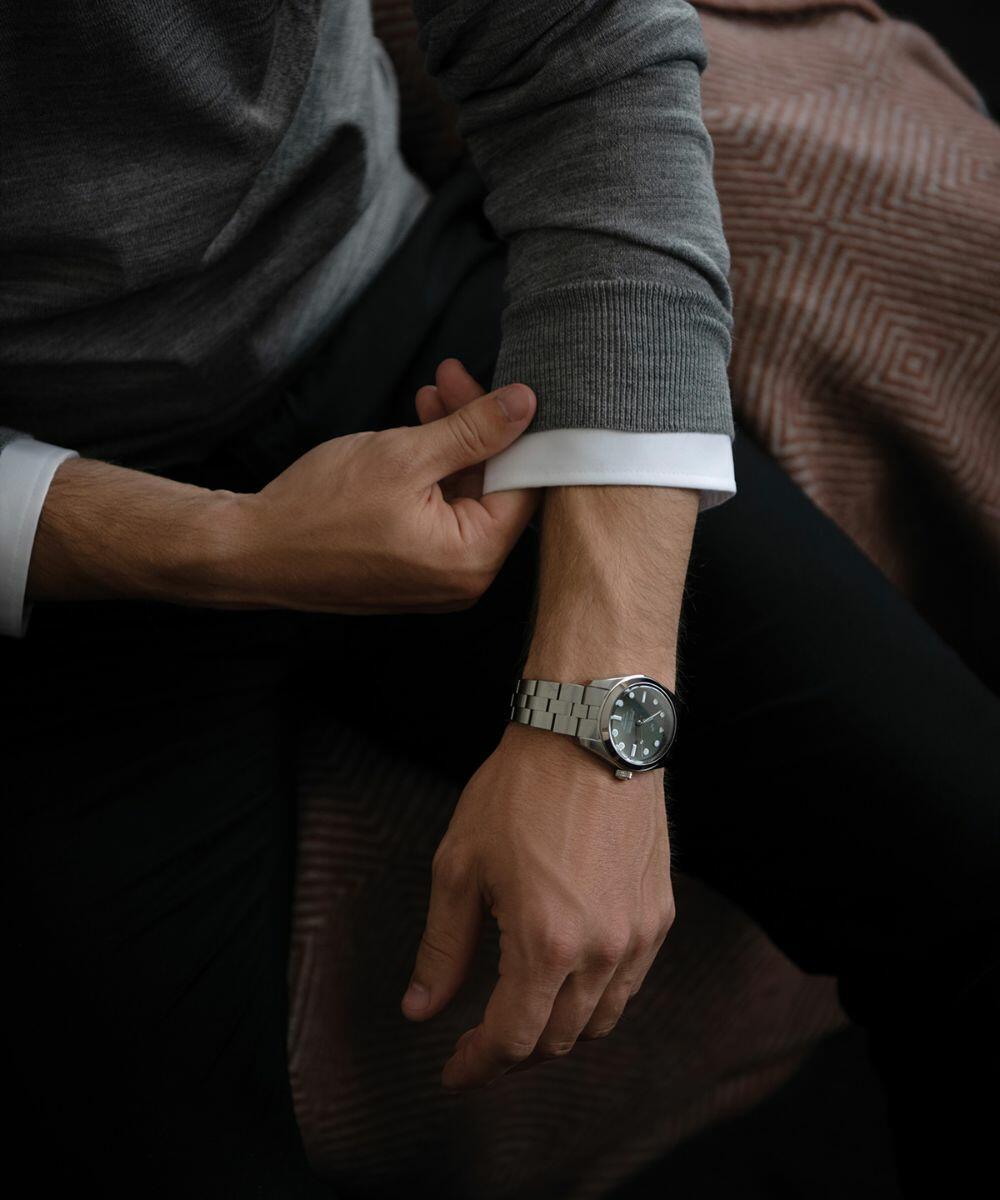 A person is adjusting the sleeve of their gray sweater, while wearing a Nimbus NB92M on their left wrist.