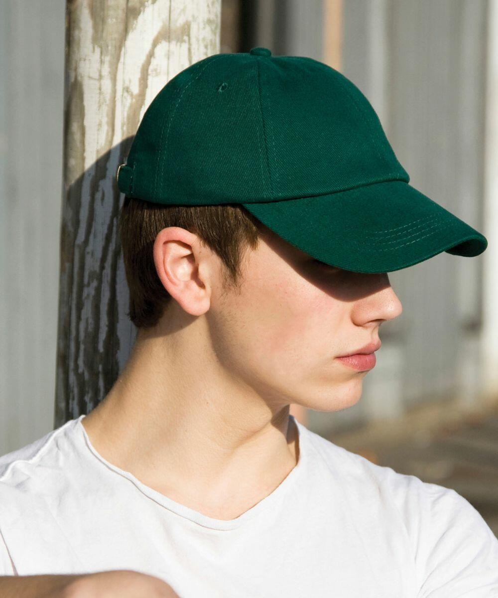Person wearing a green baseball cap and white T-shirt, looking to the side outdoors, is sporting the RC24X by Result.