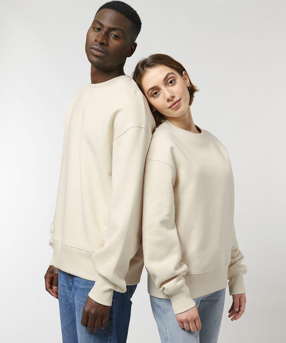 Two people wearing light-colored Stanley/Stella SX135 sweatshirts and blue jeans stand back-to-back against a plain backdrop. The person on the right leans their head on the other's shoulder.
