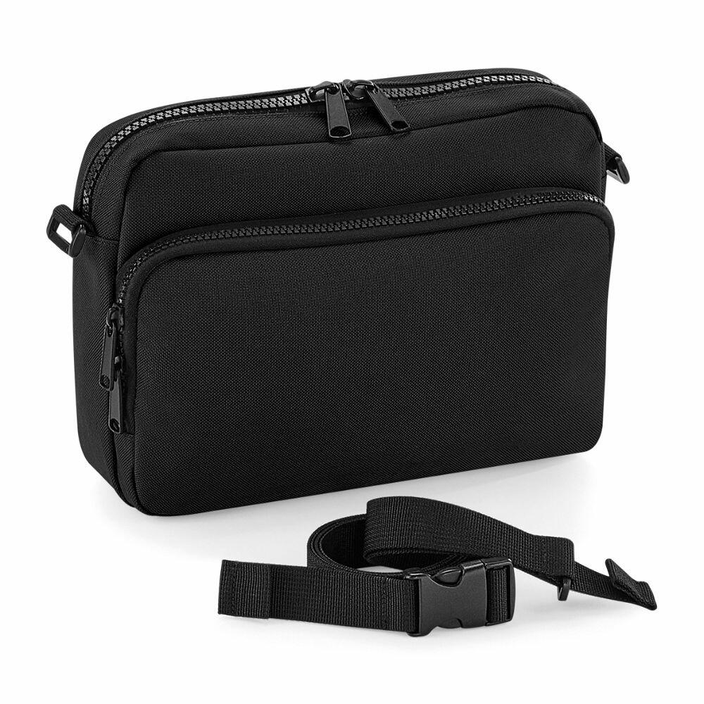 The Bagbase BG242 is a black shoulder bag featuring a zippered design and an adjustable strap at the front.