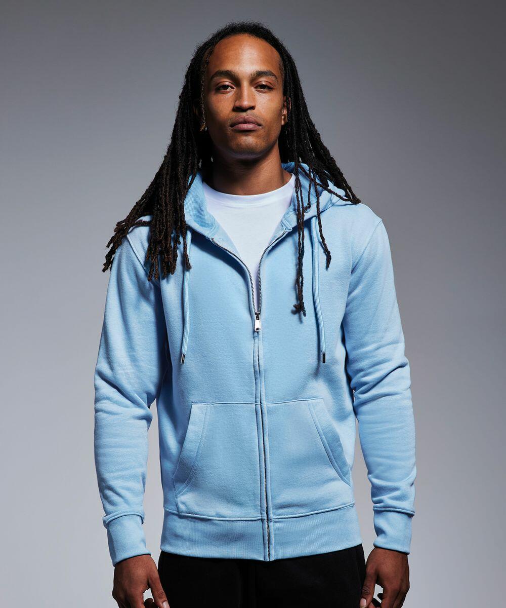 A person with long dreadlocks is wearing an Anthem AM002 light blue zip-up hoodie over a white t-shirt. They are standing against a plain grey background and looking directly at the camera with a neutral expression.