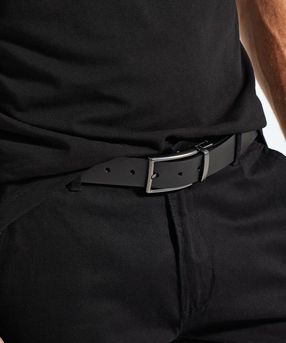 A close-up image of a person wearing black pants with an Asquith & Fox AQ904 black leather belt. The belt has a metallic silver rectangular buckle and is threaded through the belt loops of the pants. The person is wearing a black shirt tucked into the waist of the pants.