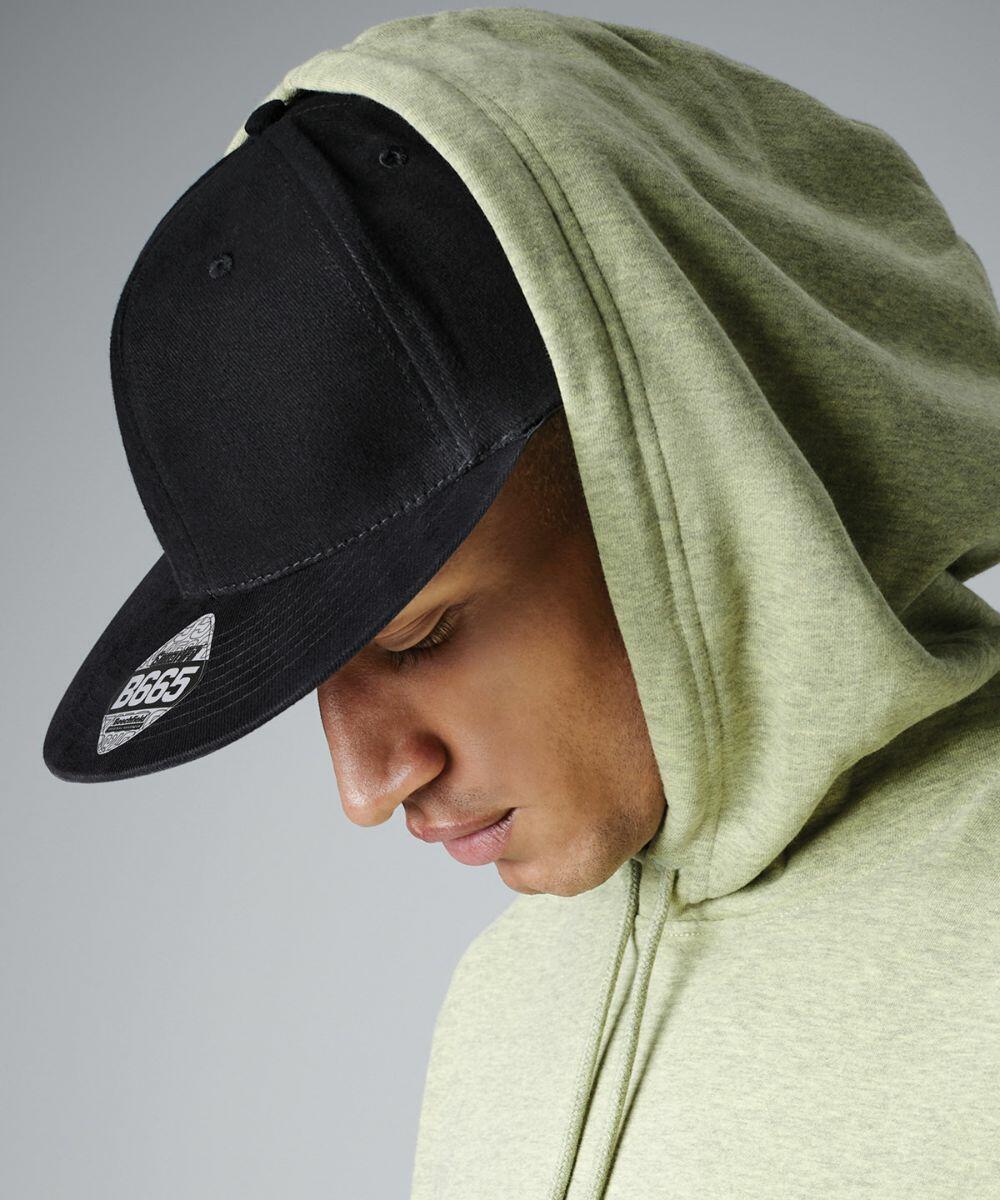 A person wearing a light green hoodie and a black Beechfield BC665 baseball cap looks down, with the hood pulled up over their head. The background is a plain grey. The cap has a sticker on the bill.