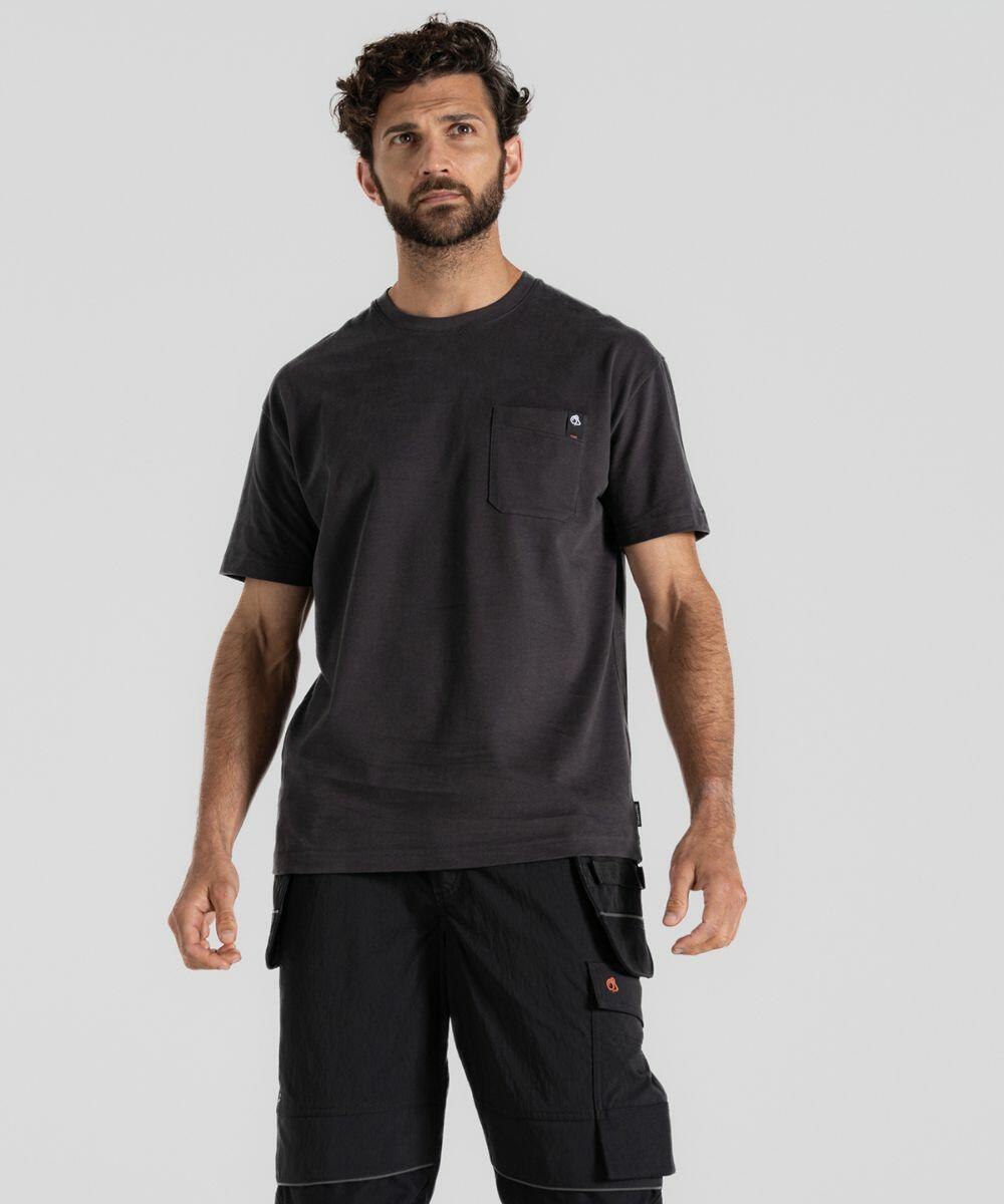 A man with short curly hair and a beard is wearing a black Craghoppers CR704 T-shirt with a small chest pocket and black cargo shorts, standing against a plain gray background.