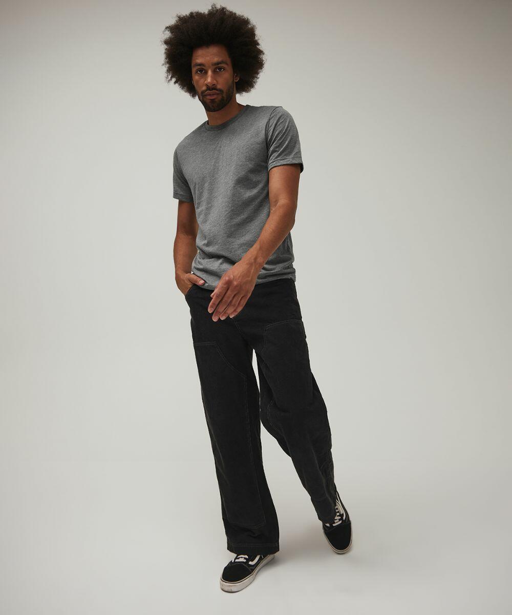 A man with an afro hairstyle wearing a gray Bella + Canvas CV003 T-shirt, black pants, and black sneakers is posing against a plain background.