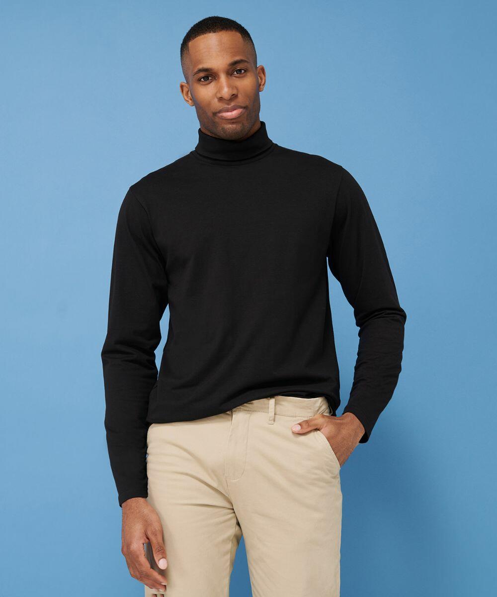 A man wearing a black Henbury HB020 turtleneck and beige pants poses against a blue background.