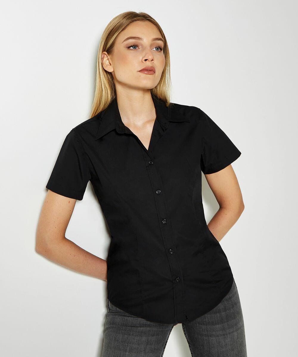 A person stands against a white background, wearing a Kustom Kit KK728 short-sleeve black button-up shirt and dark jeans.
