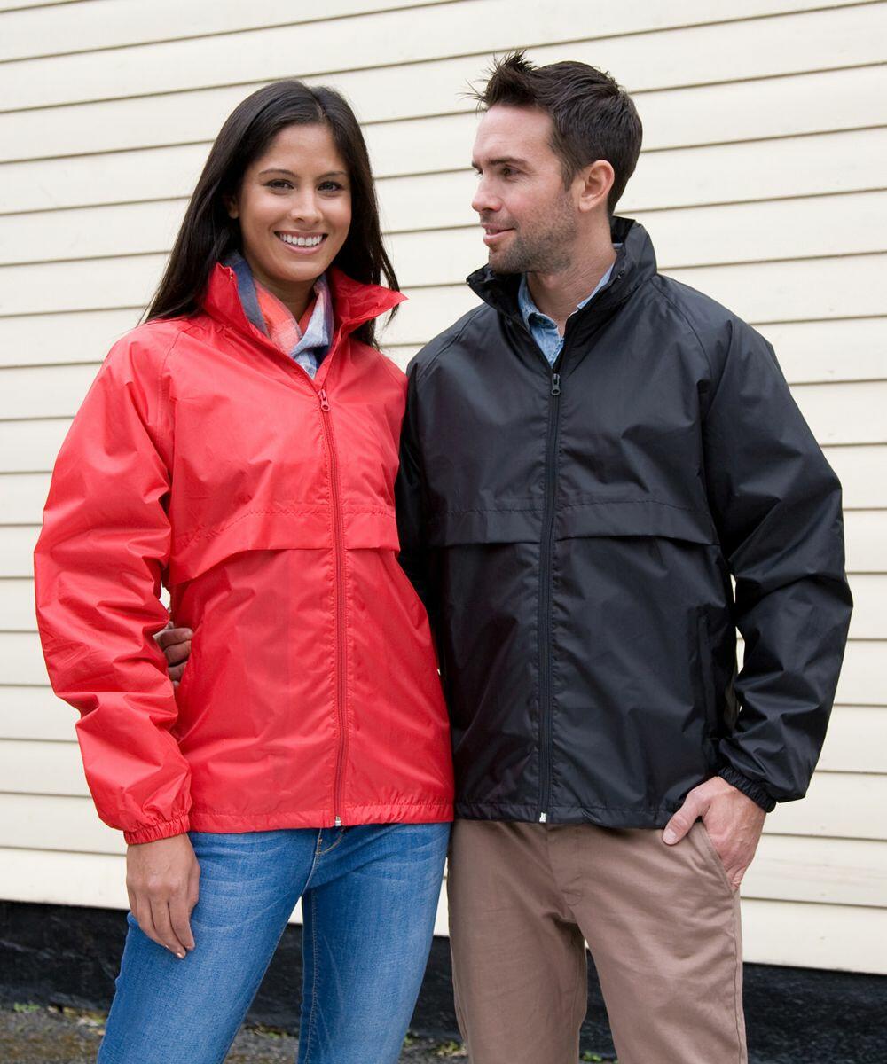 A woman in a Result R205X red jacket and a man in a Result R205X black jacket stand together in front of a beige wall.