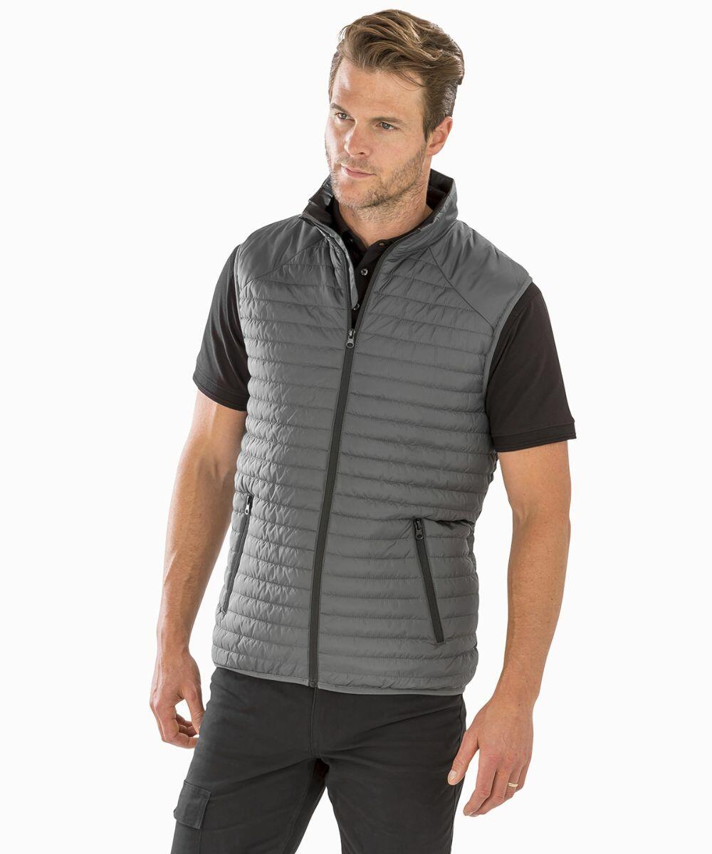 A man wearing a gray, zip-up, padded Result R239X vest over a black short-sleeved shirt stands against a plain white background. He has short hair and a neutral expression.